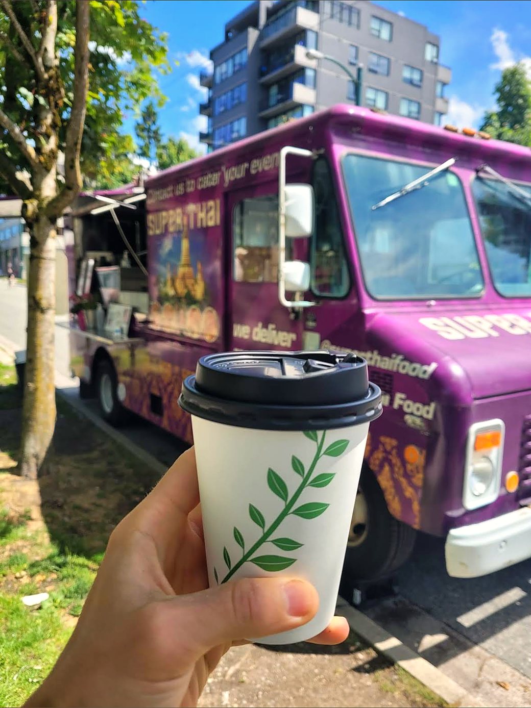A drink in hand in front of the Super Thai truck on a sunny day