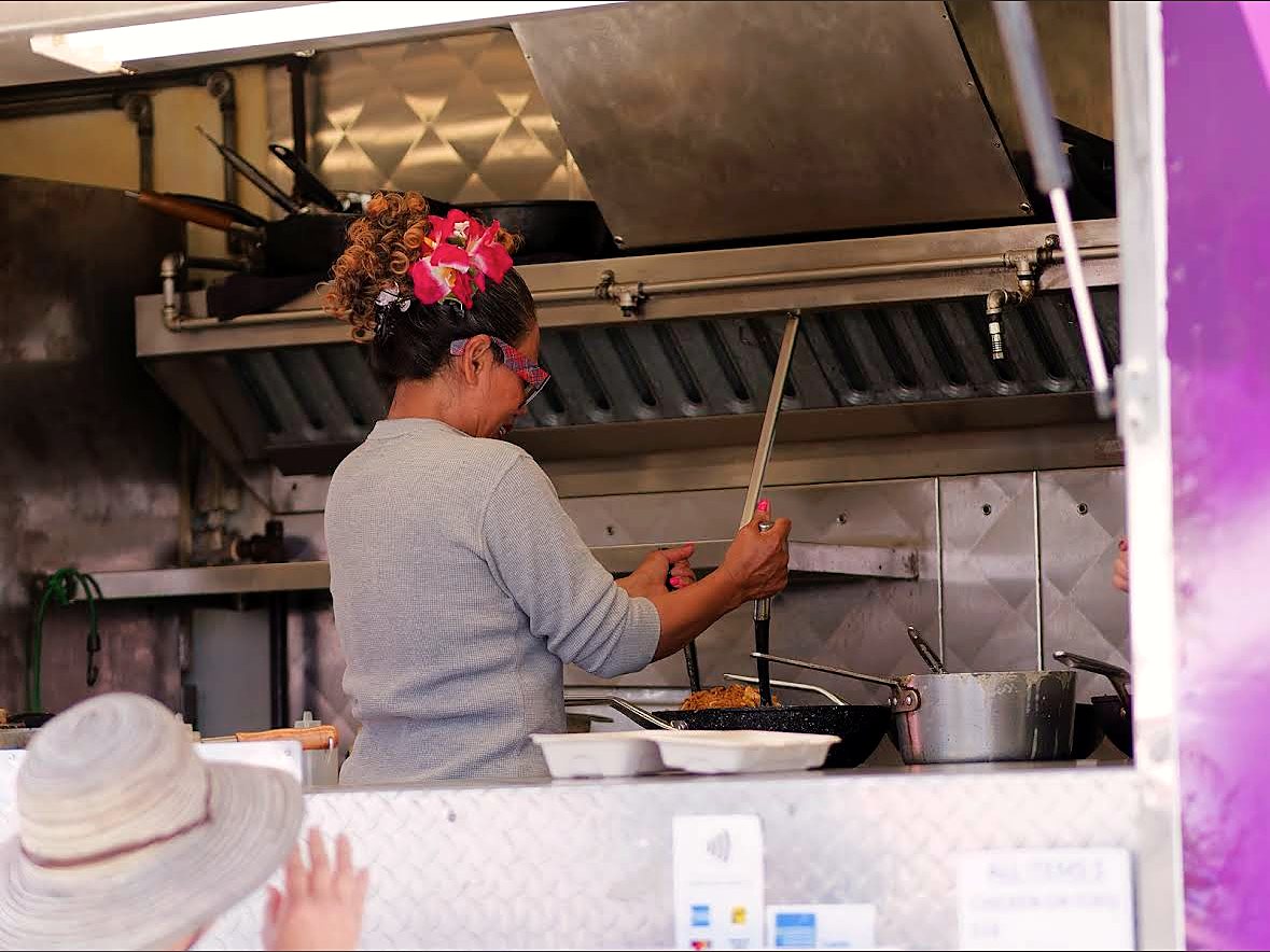 One of the cooks stir-frying in the truck with a pink orchid in her hair