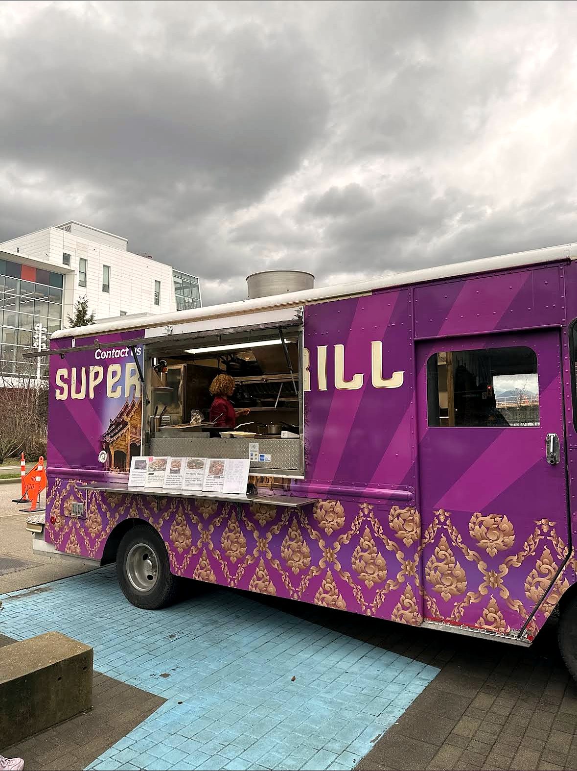 The purple and gold Super Thai food truck parked under a dramatic Vancouver sky